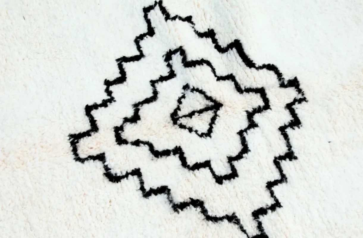 Close‑up photo illustrating what is a Berber rug: hand‑knotted Beni Ourain diamond pattern in black wool on a cream background.