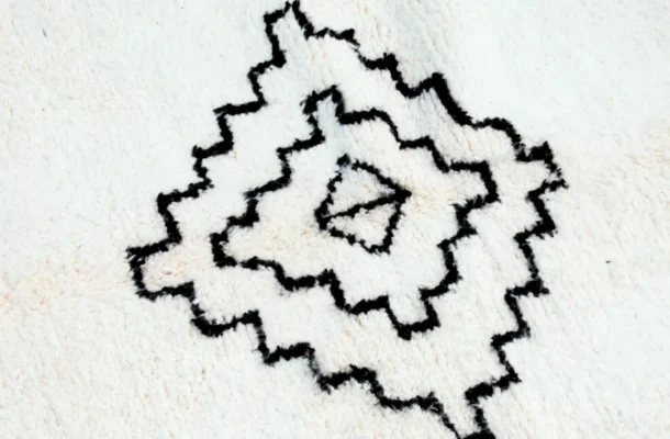 Close‑up photo illustrating what is a Berber rug: hand‑knotted Beni Ourain diamond pattern in black wool on a cream background.