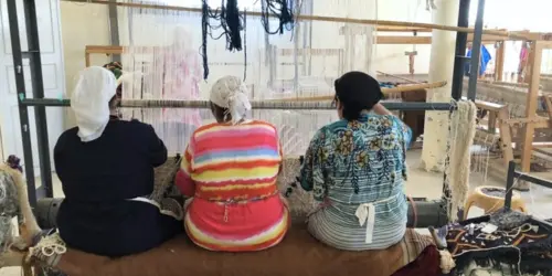 Three Berber women weaving a handmade wool rug on a traditional loom as part of Moroccan rug making
